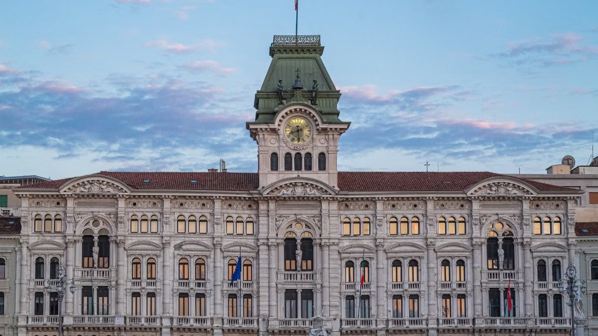 Neoclassical architectural landmark in Trieste, Italy, with clock tower against blue sky at dusk.